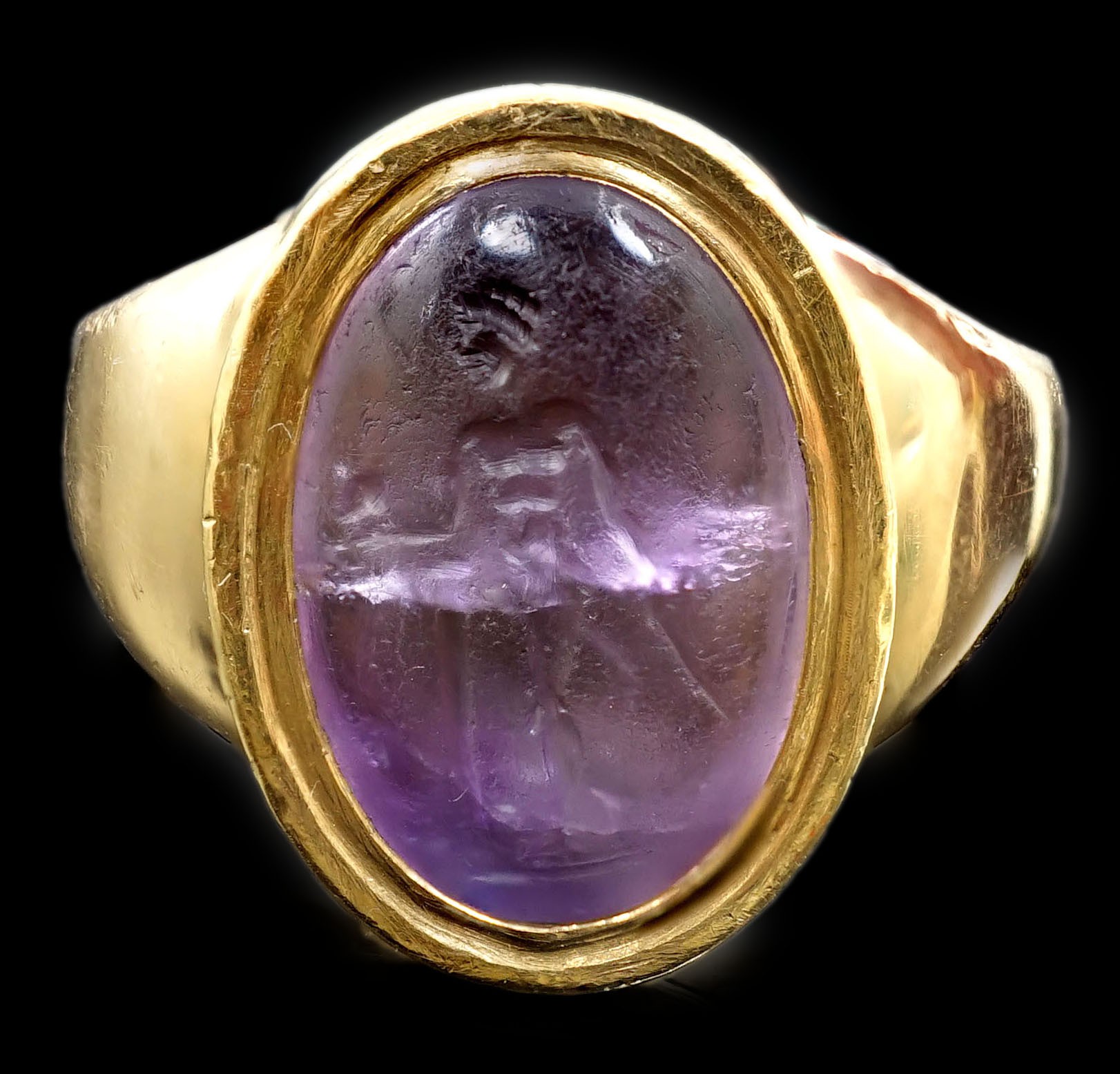 A Roman oval intaglio amethyst, carved with a figure with staff and pedestal, set in a later heavy gold ring mount